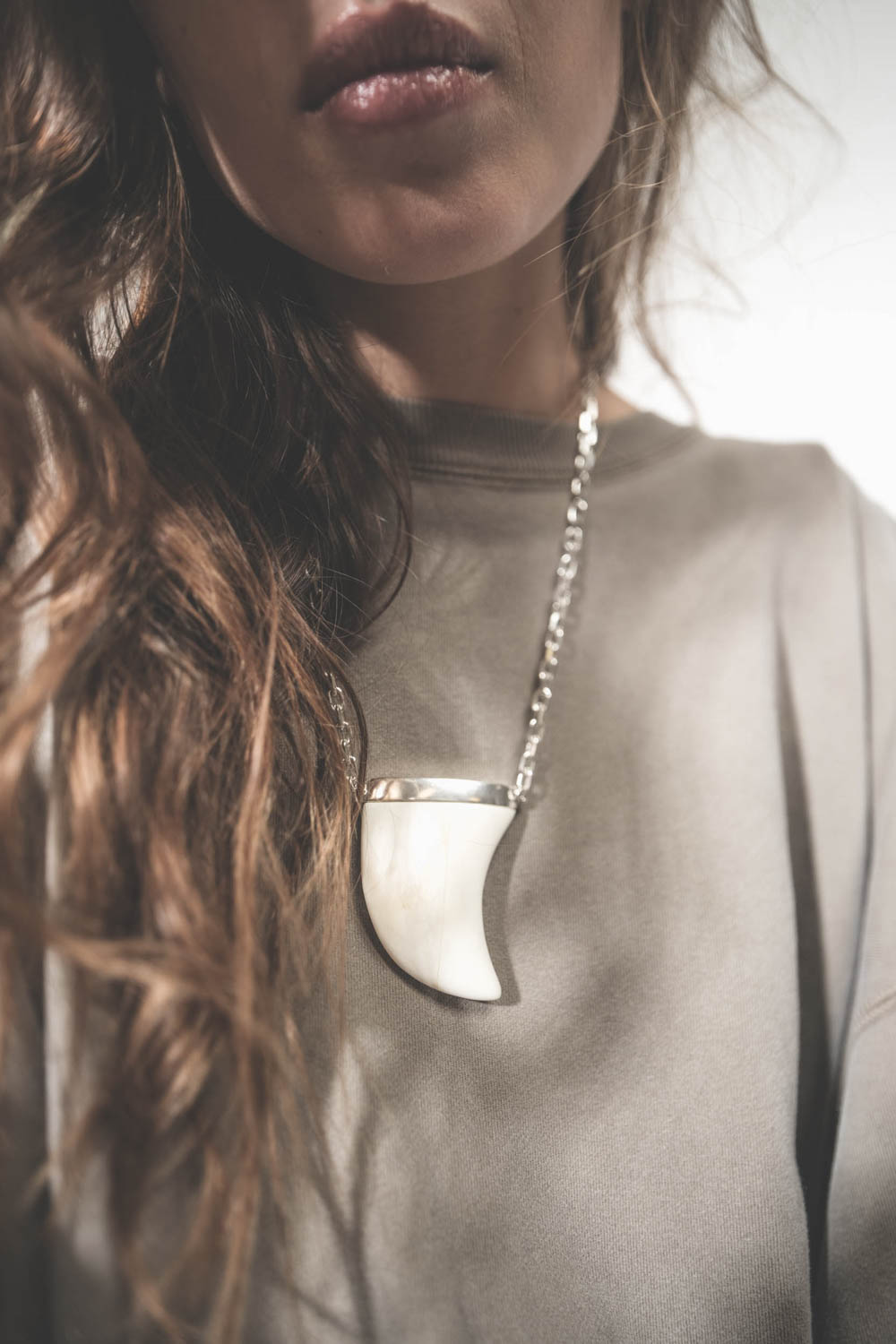 Collier oversize dent de requin en os écru sur chaine argent Ellen Isabel Marant. Porté sur un sweat-shirt kaki.