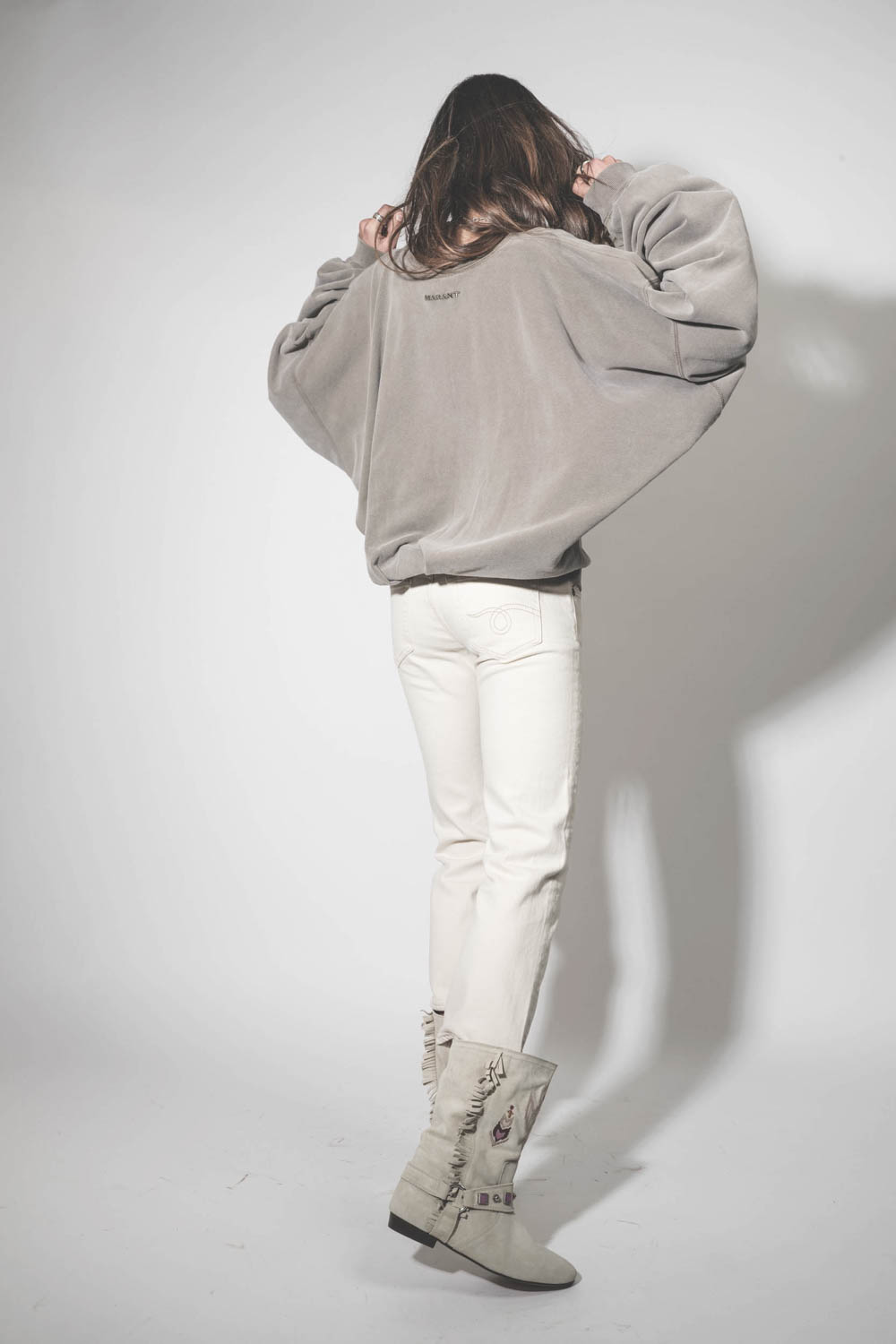 Jean taille basse Skinny Boy Straight écru stretch R13. Porté de dos avec des bottes en cuir suédé écru brodées.