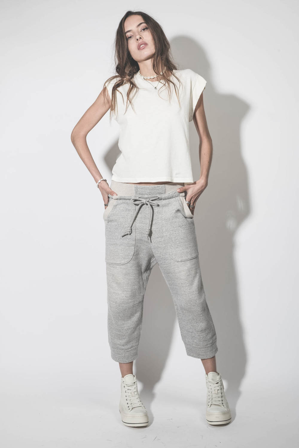 Tee-shirt court sans manches écru Peak Shoulder The Great. Porté de face avec un bas de jogging oversize.