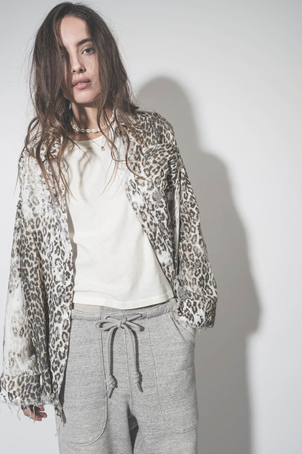 Tee-shirt court sans manches écru Peak Shoulder The Great.  porté avec un collier coquillage. 